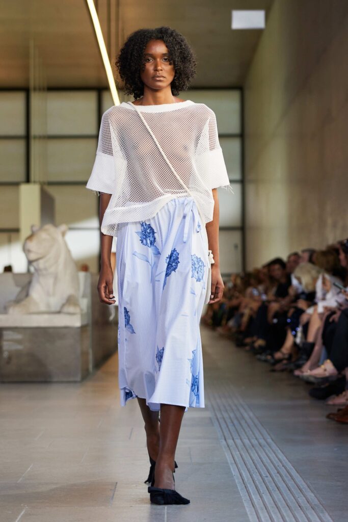 An oversized mesh top paired with a pleated blue and white skirt featuring floral designs.