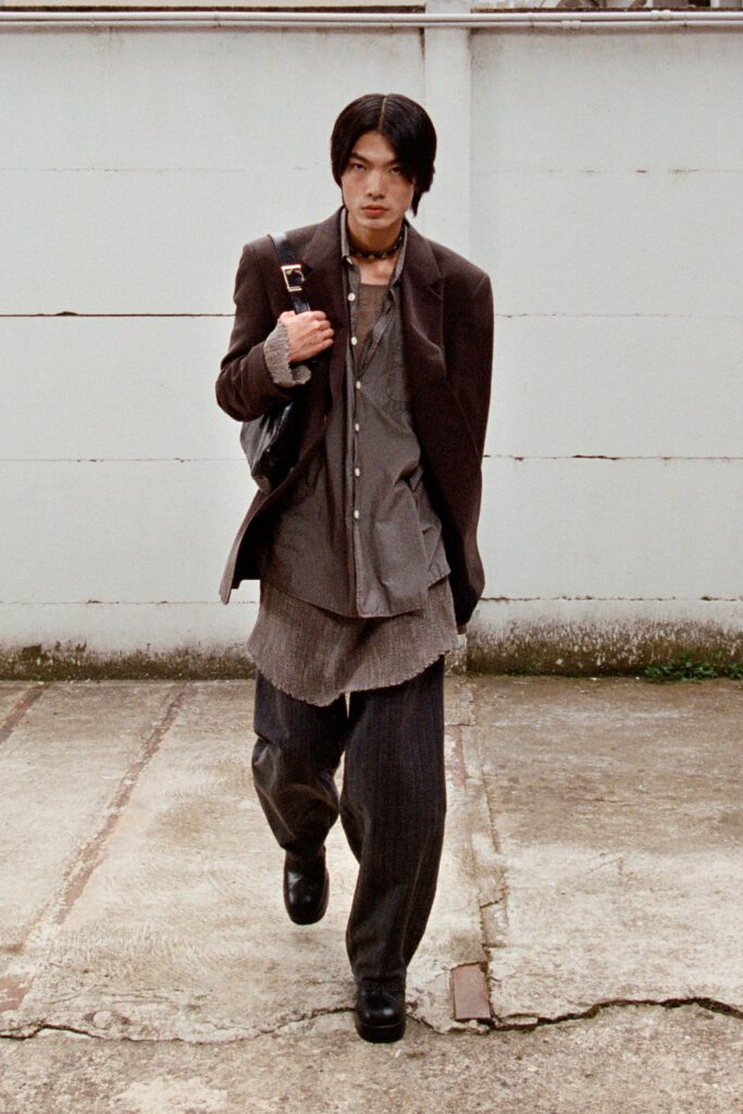 A relaxed brown jacket layered over a gray collared shirt with long sleeves and striped details.