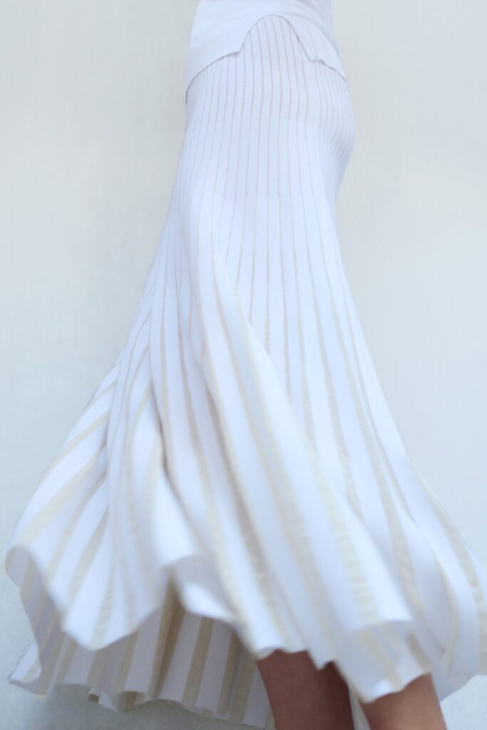 A fitted white sleeveless dress with a V-neckline and pleated A-line silhouette.