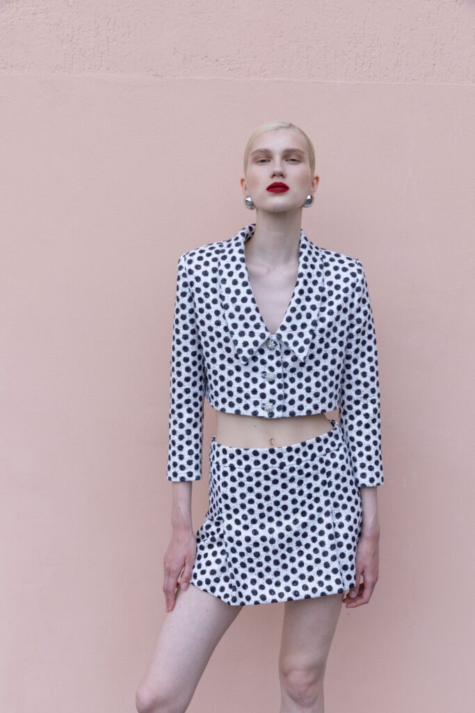 A fitted white and black polka-dot blazer with a matching skirt, featuring long sleeves and a collared design.