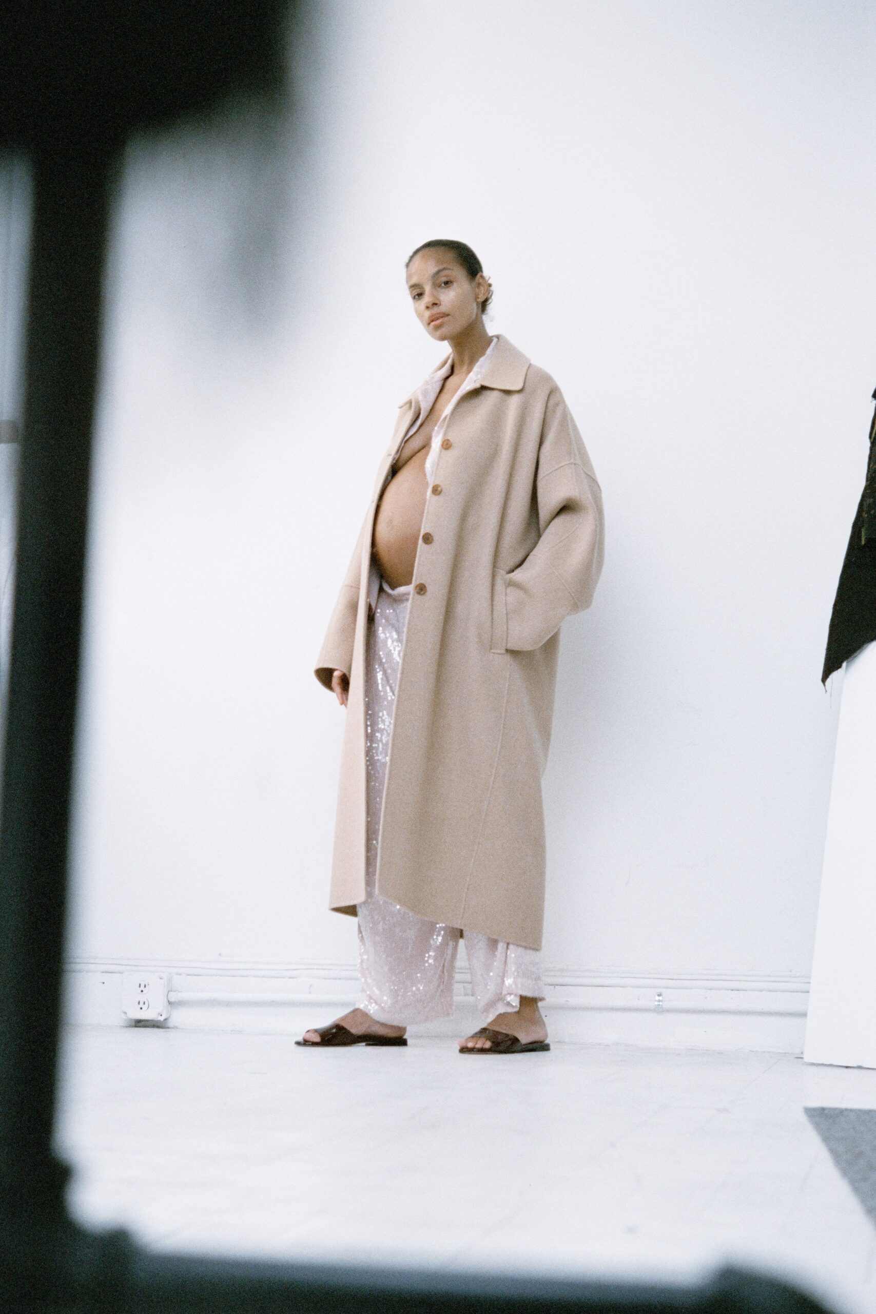 An oversized beige coat paired with silver sequined pants, featuring a collared design and buttoned front.