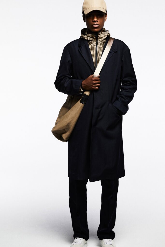 A relaxed black coat paired with beige pants and a collared shirt underneath.