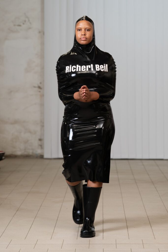 A fitted black latex long-sleeve dress featuring a high neckline and knee-length hem.