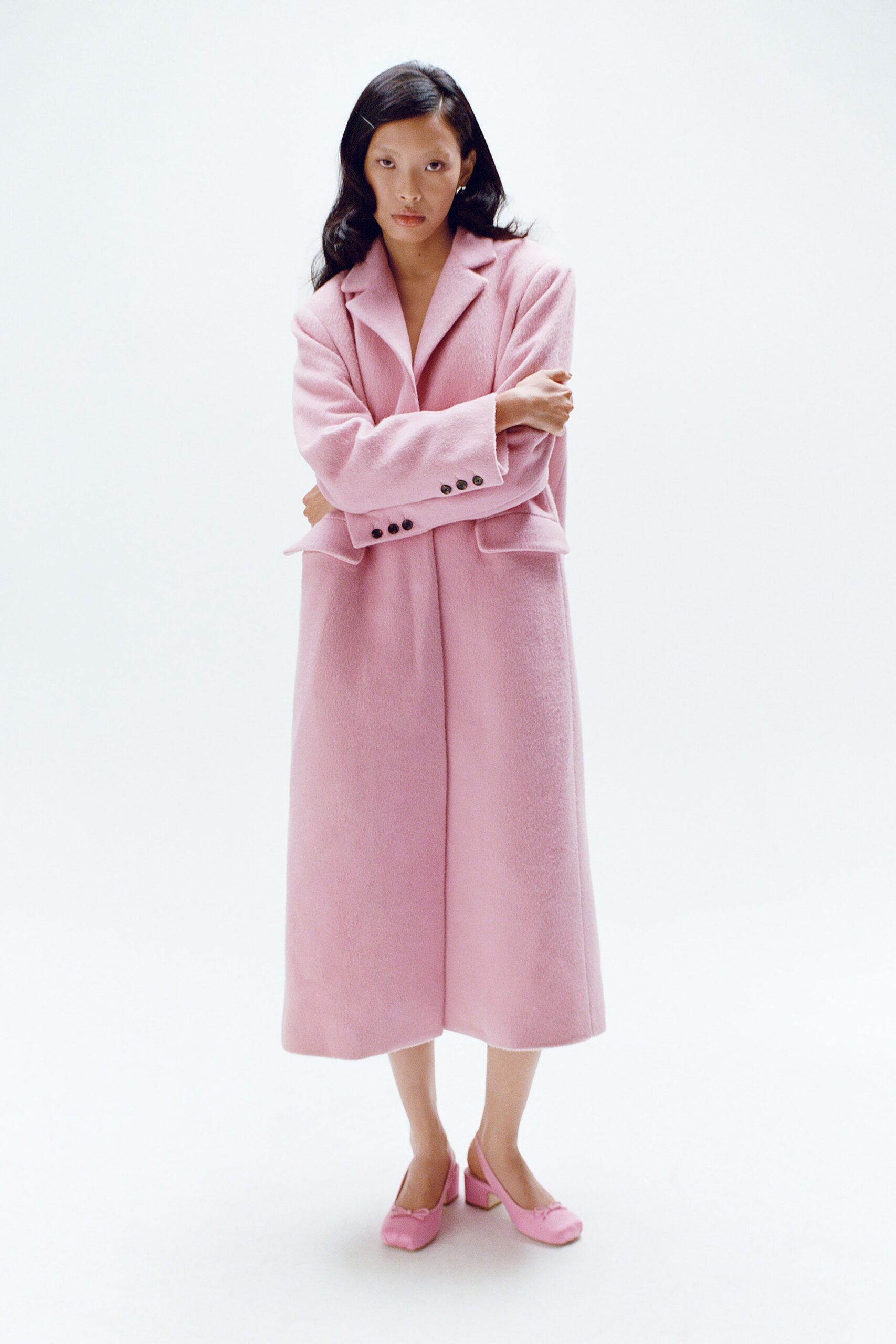A relaxed pink wool coat with long sleeves and a collared design, featuring button details.