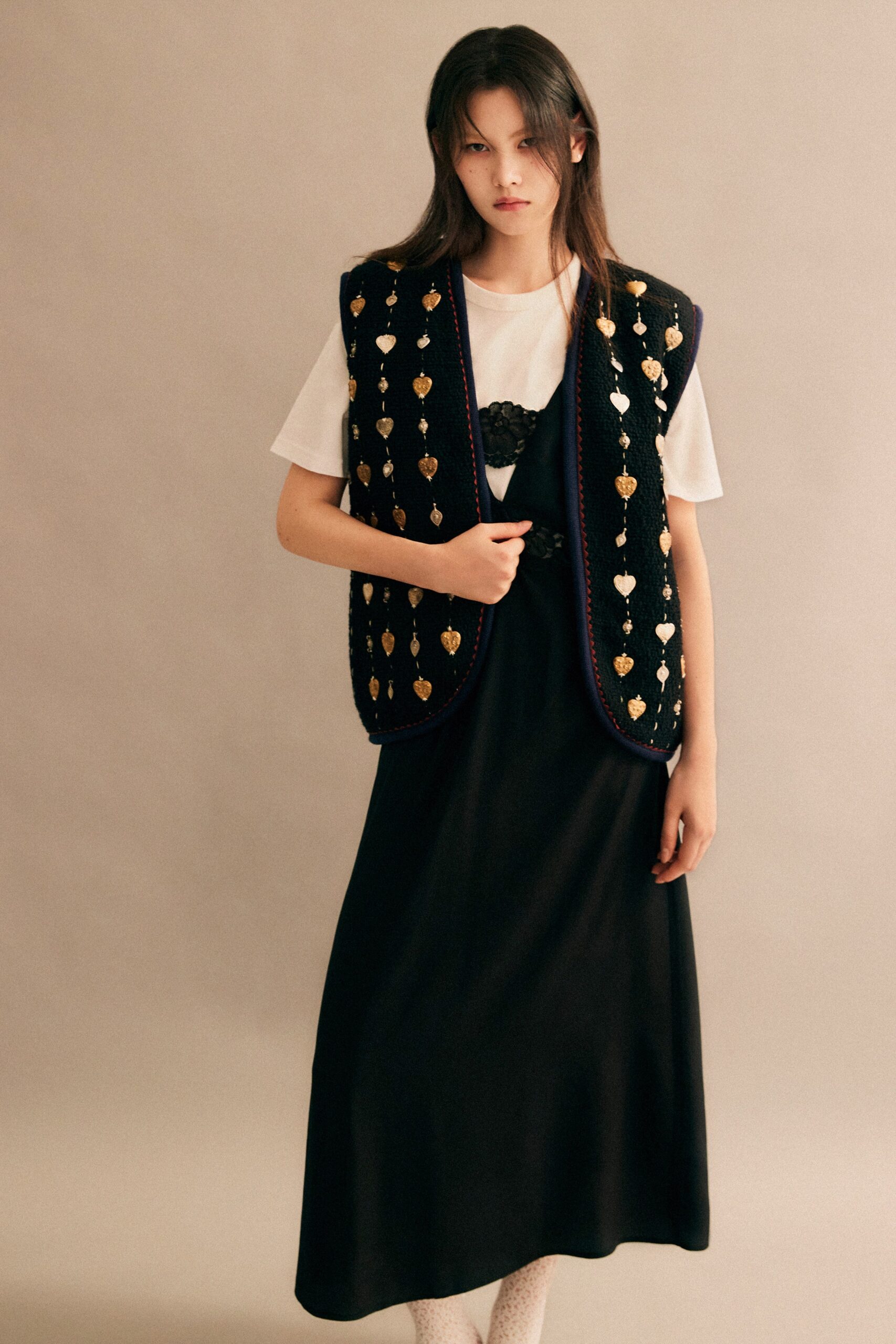 A fitted black dress layered with a decorative vest over a white top.
