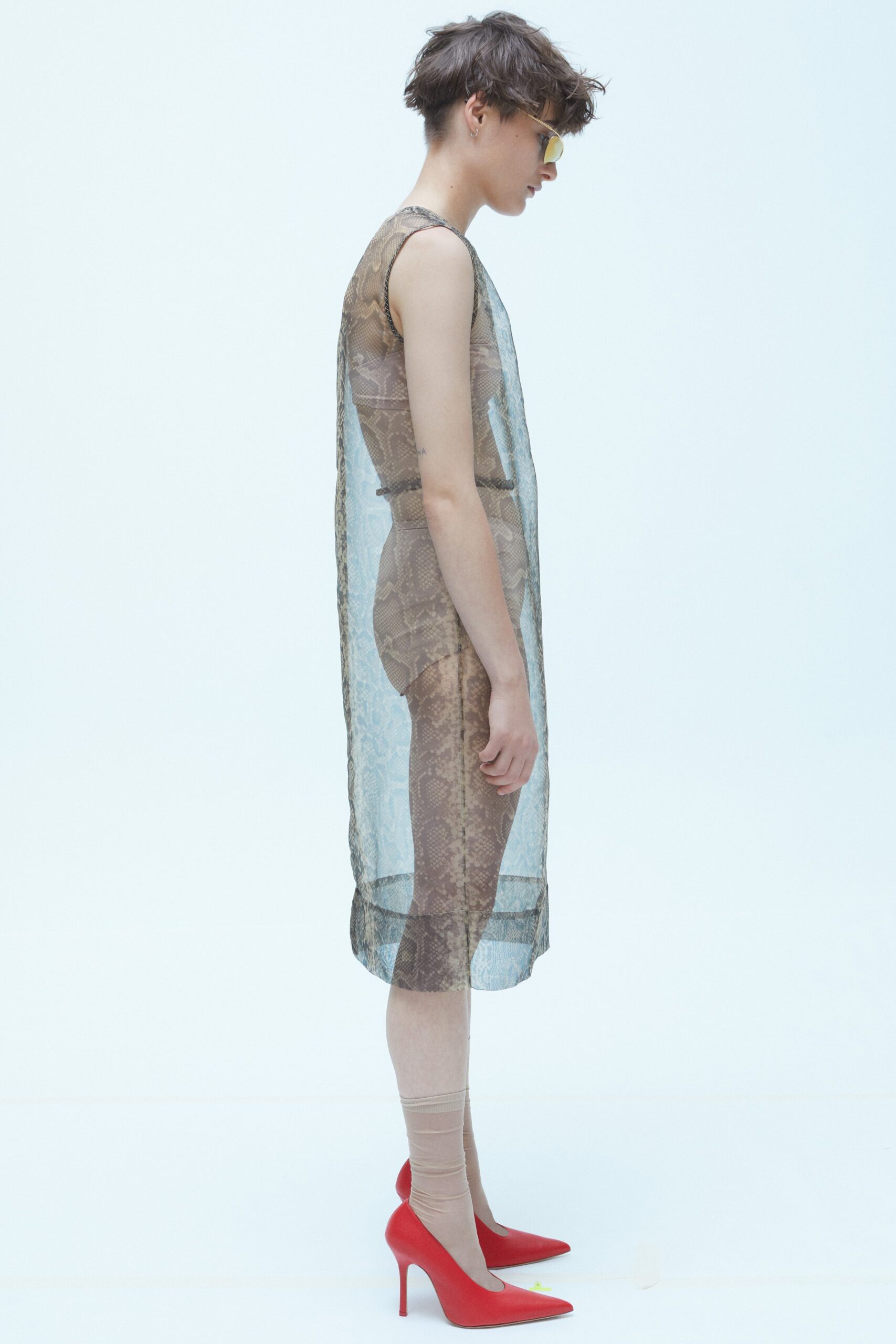 A fitted beige sheer sleeveless dress with a high neckline and layered design.