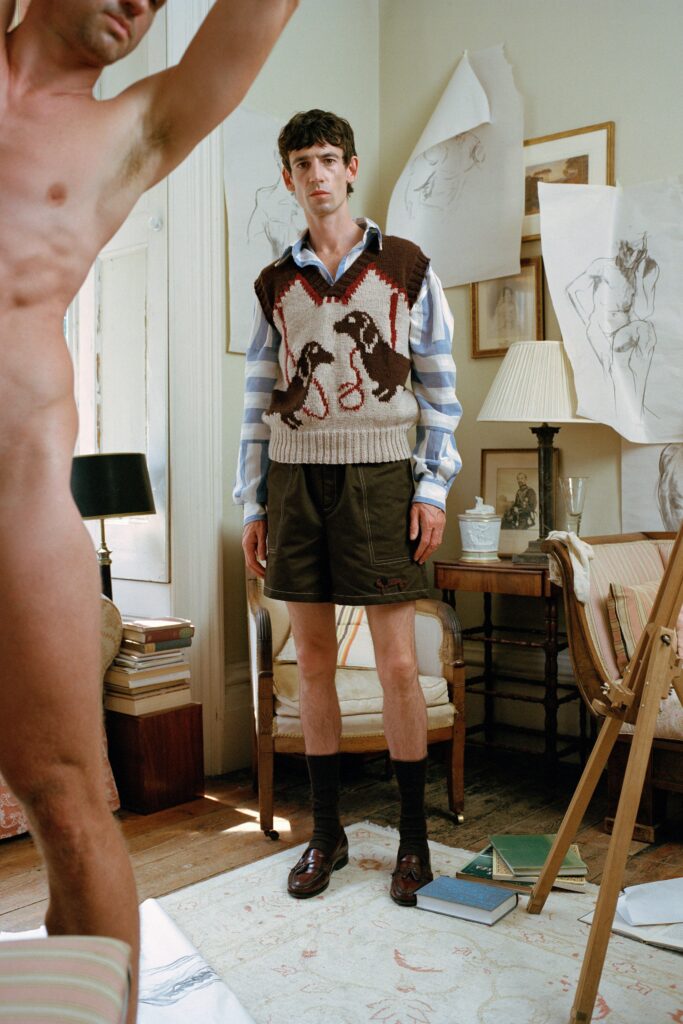 A fitted brown vest layered over a collared striped shirt and paired with shorts.