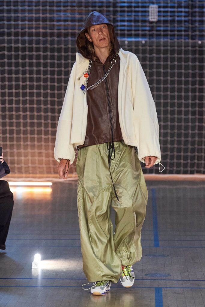 A relaxed brown leather hooded jacket paired with wide-leg green pants.
