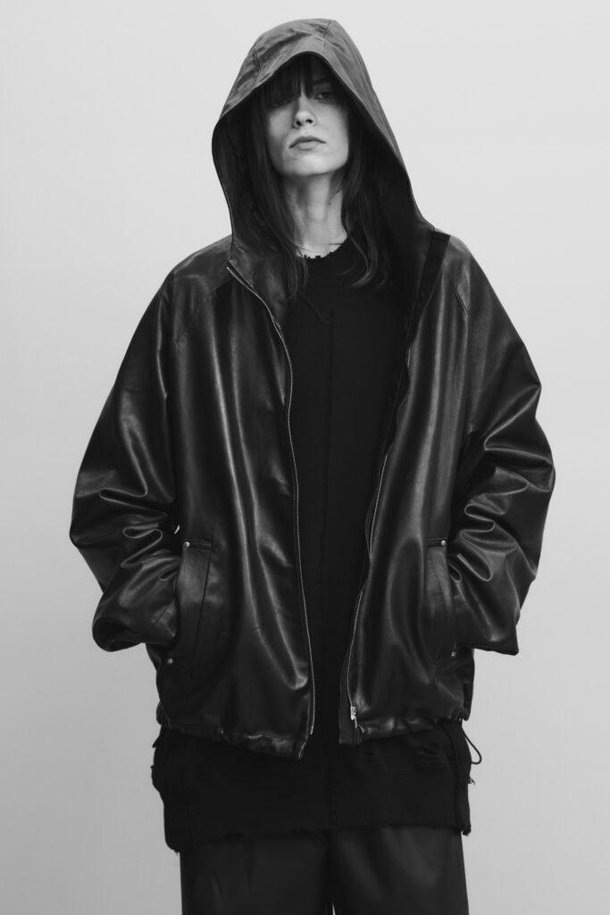 An oversized black leather jacket with a hood, paired with a black top underneath.