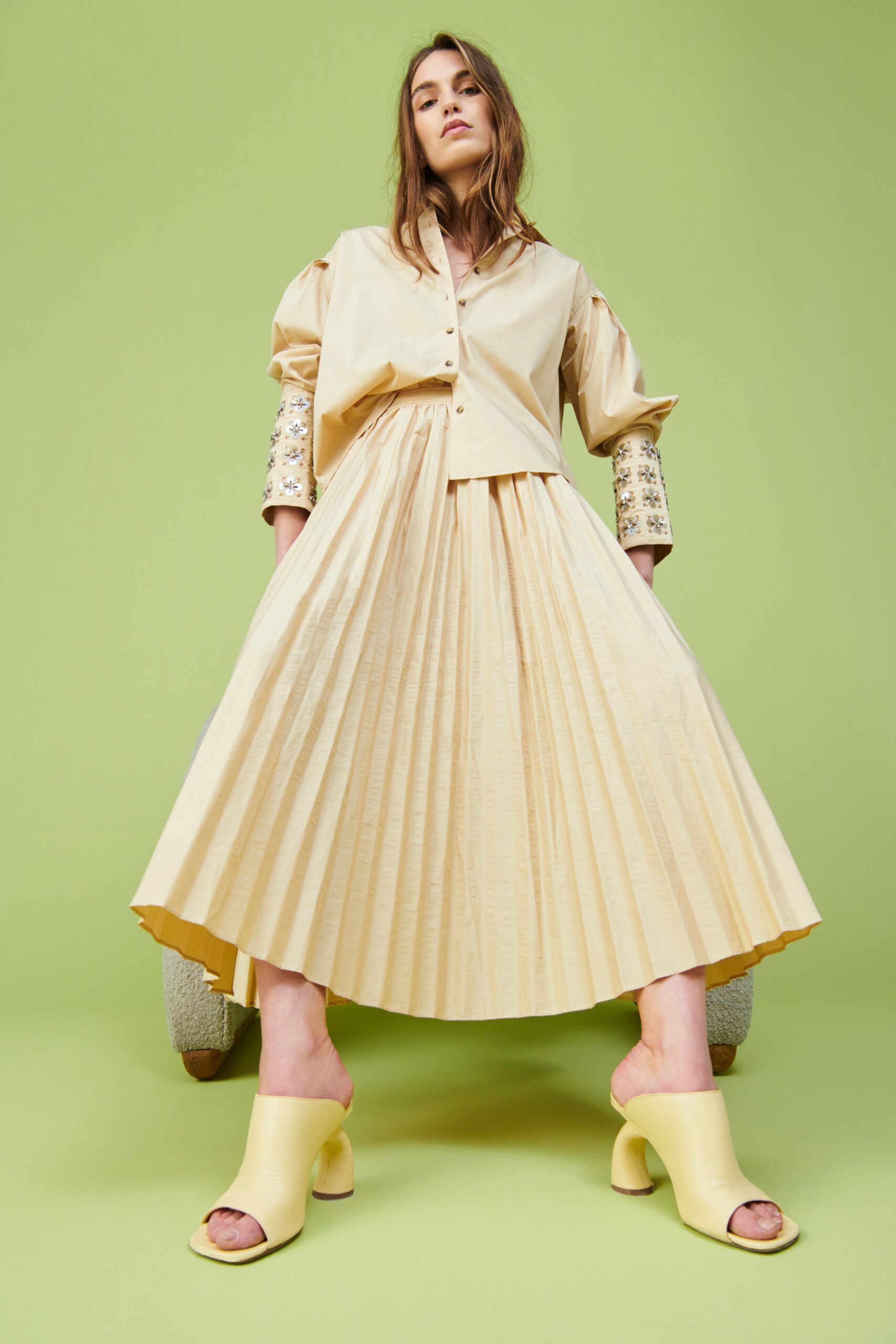 A fitted beige cotton dress with pleats, complemented by a long-sleeve collared shirt.