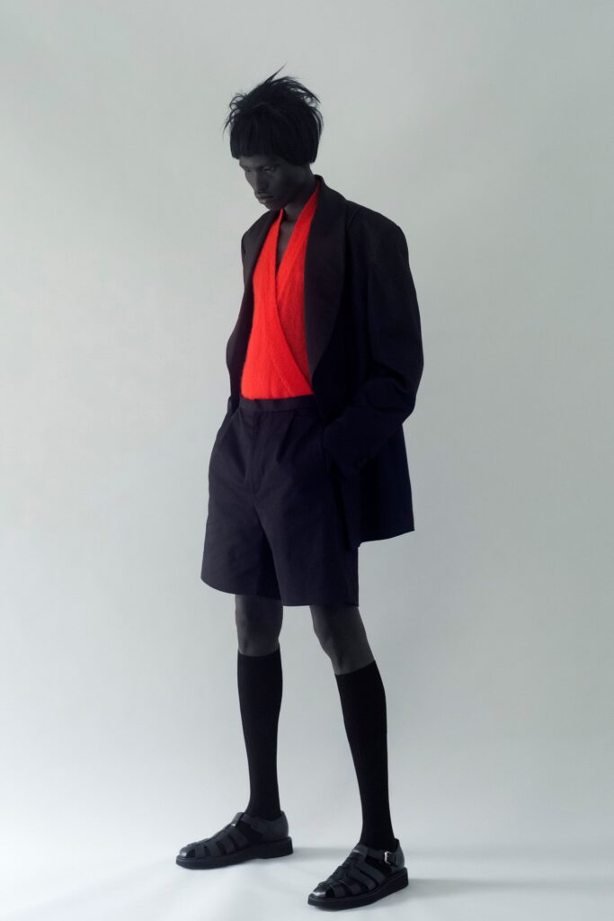 A relaxed black jacket paired with a red top and black shorts featuring an asymmetric design.
