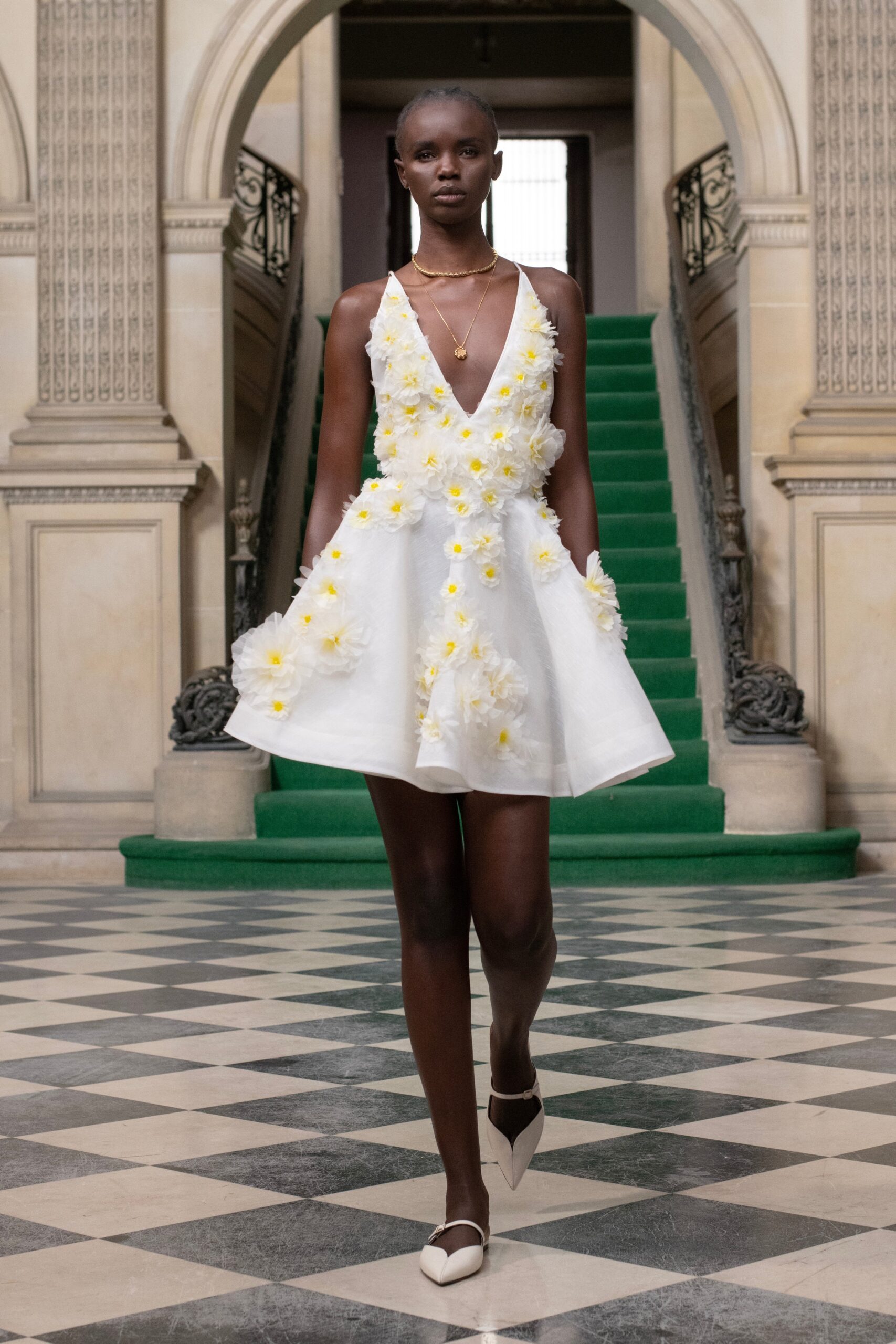 A fitted white sleeveless dress with a V-neckline and flared silhouette adorned with floral details.