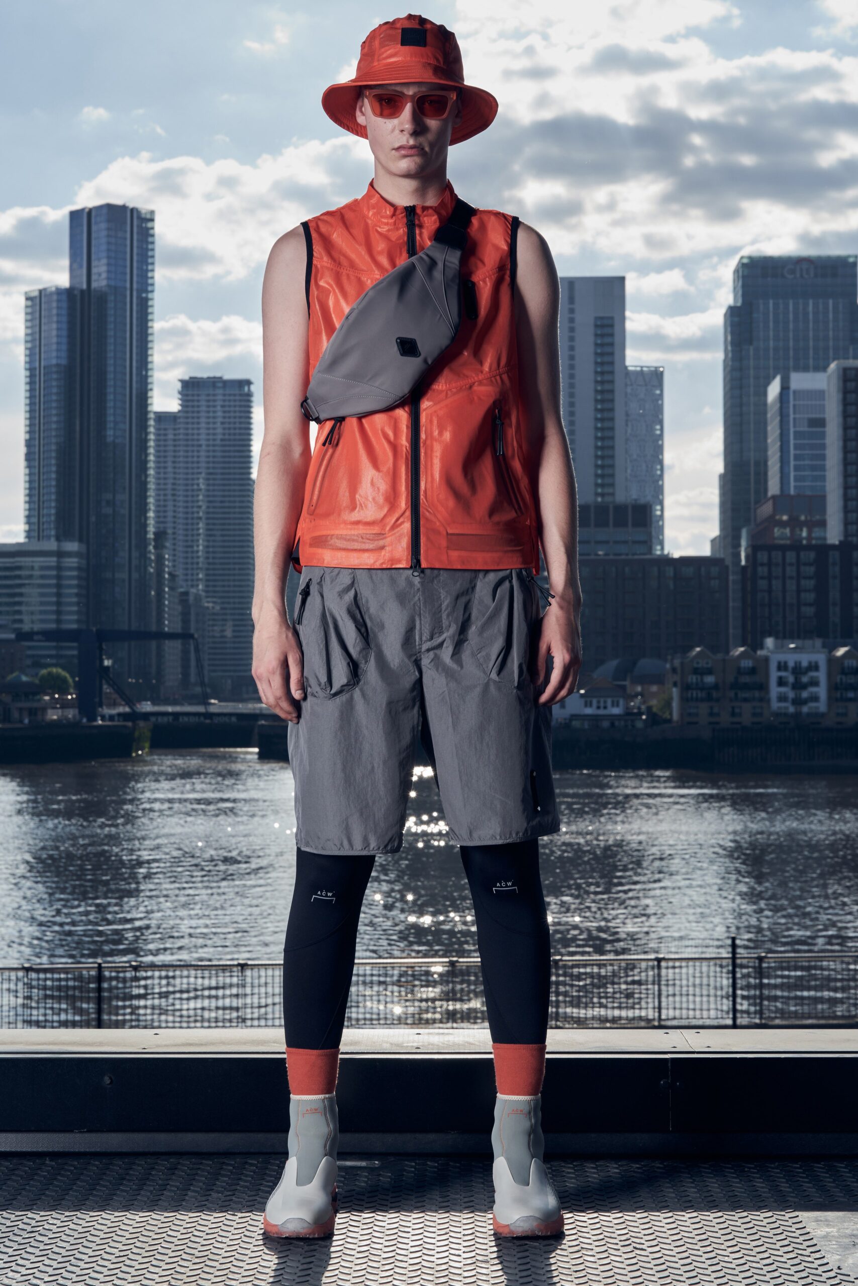A fitted orange leather sleeveless vest paired with gray pleated shorts.