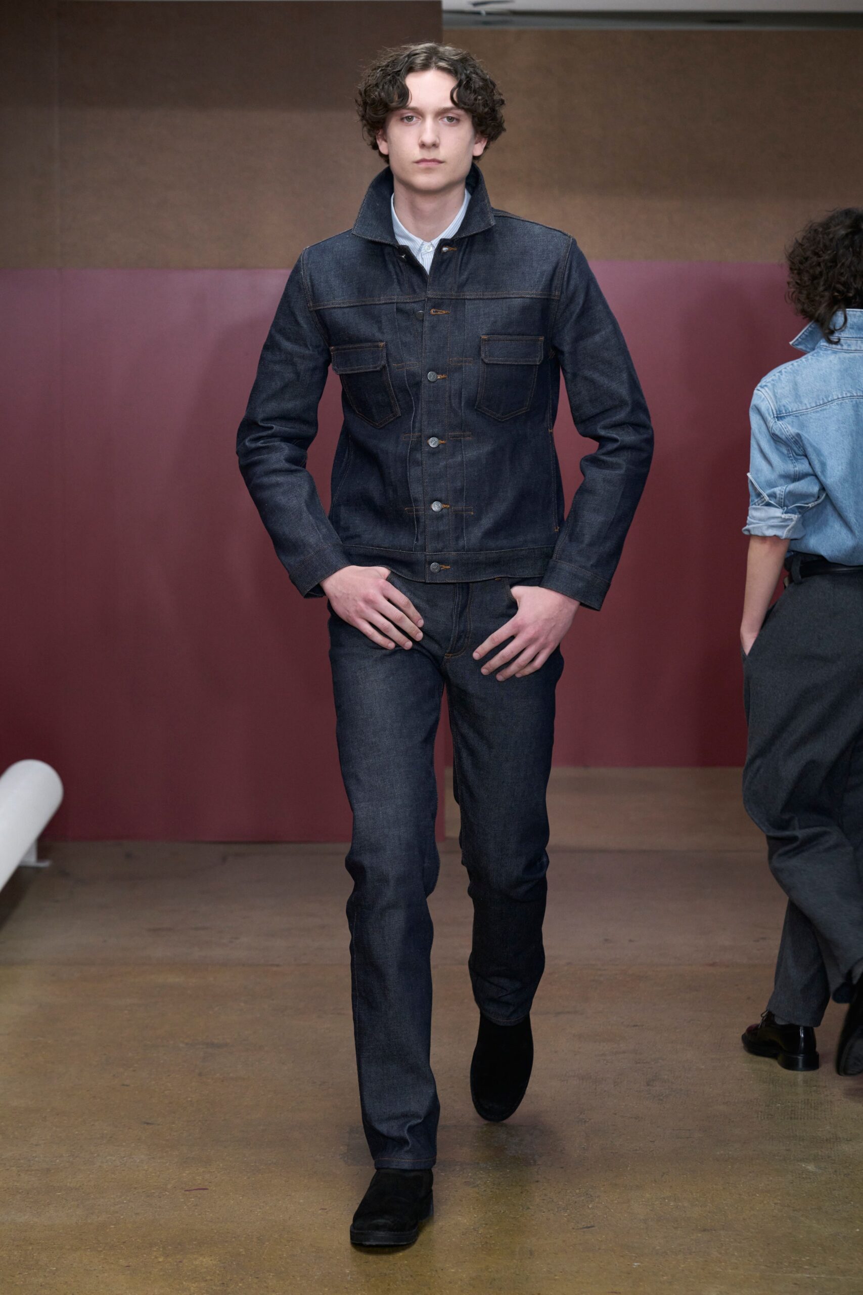 A fitted blue denim jacket with long sleeves and collared neckline paired with straight-leg denim pants.