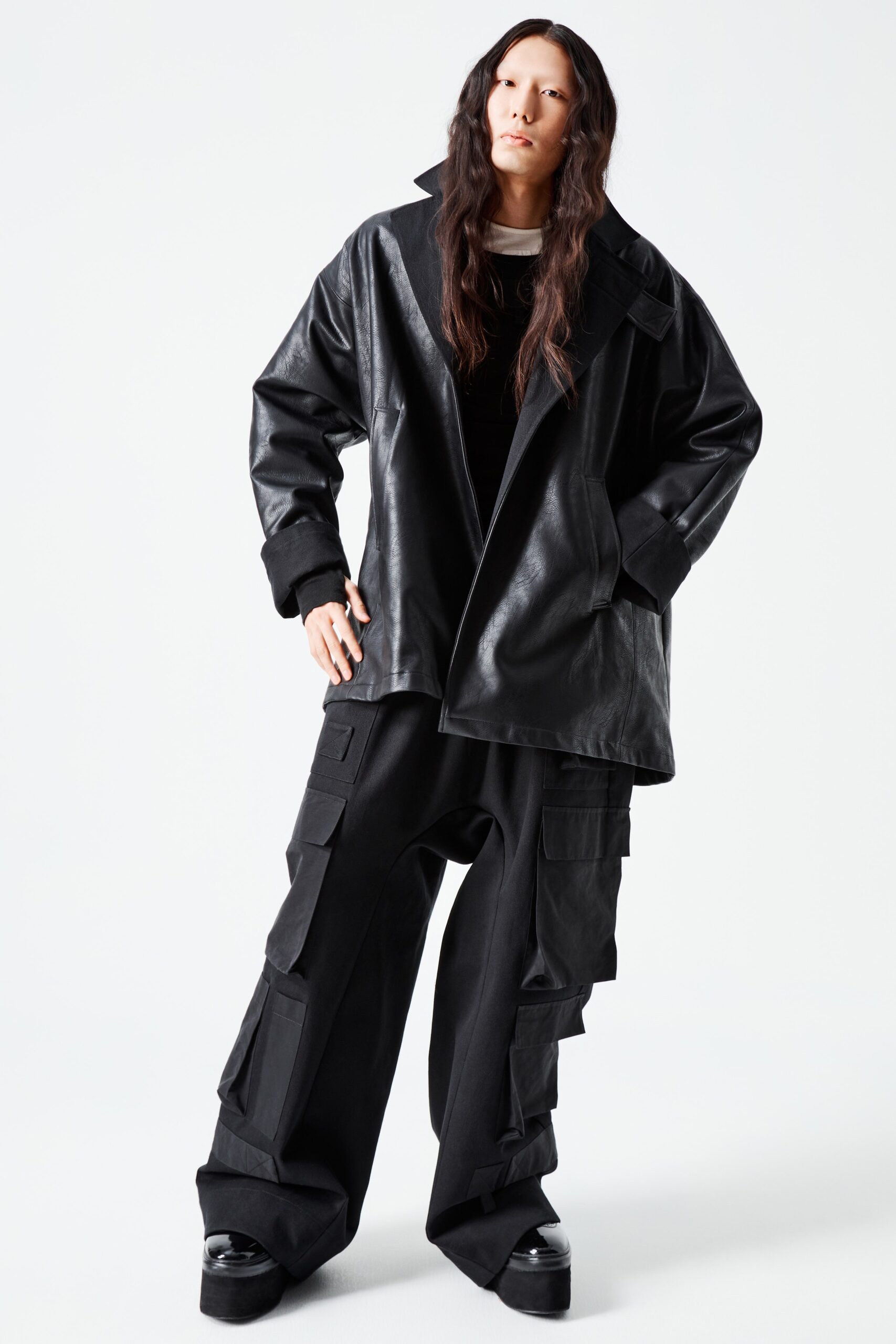 This ensemble features a relaxed black leather jacket with a striking collared design, complemented by wide-leg pants that enhance the overall silhouette. The asymmetric detailing on the pants adds a contemporary edge, creating a bold statement that balances structure and fluidity.