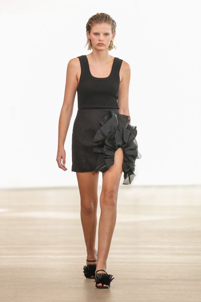 A fitted black sleeveless dress with an asymmetric design and pleated details.