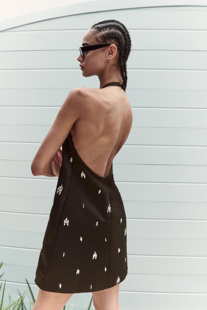 A fitted black sleeveless dress with an embroidered design and a backless construction.