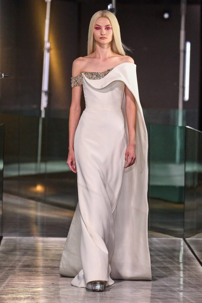 A fitted white silk off-shoulder gown with a draped design detail.