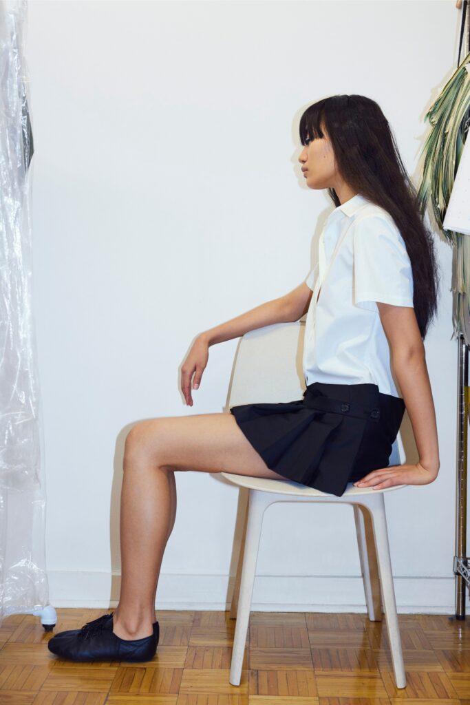 A fitted white collared shirt paired with a black pleated skirt, creating a stylish look.