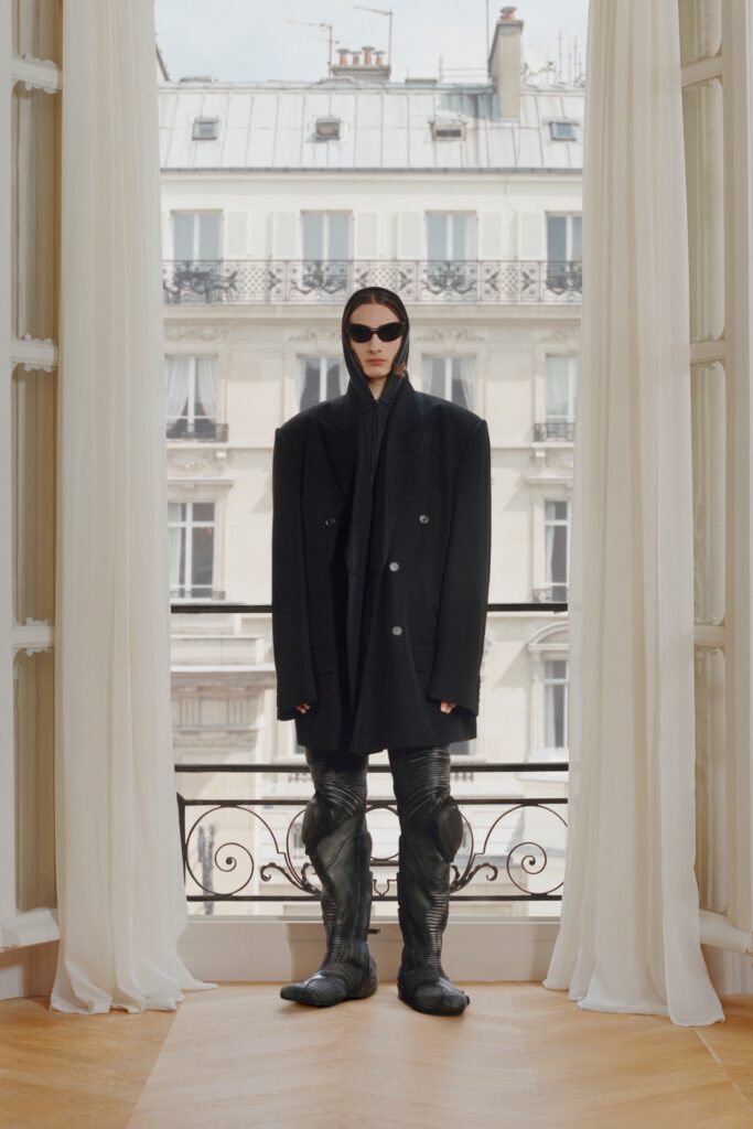 An oversized black wool coat with long sleeves and collared design, paired with matching pants.