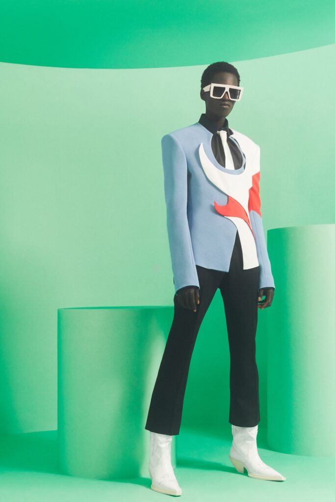 A tailored blue blazer with asymmetric design paired with black pants and white boots.