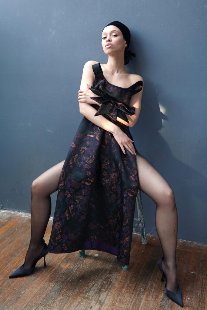 A fitted black silk sleeveless dress with an off-shoulder design and asymmetric silhouette.