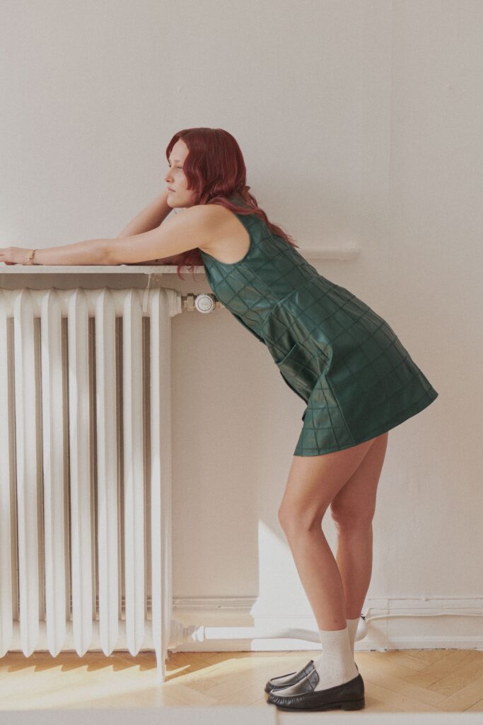 A fitted green leather mini dress with a sleeveless design and high-neck construction.