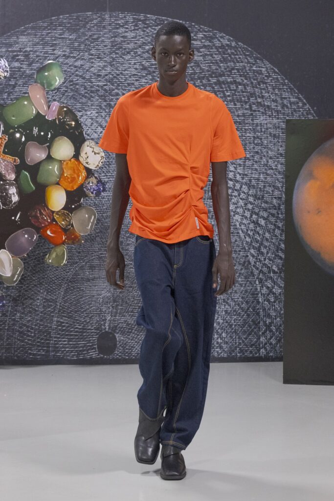 A relaxed orange t-shirt with an asymmetric design paired with blue denim pants.