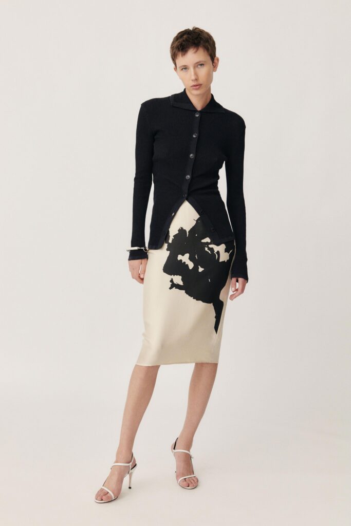 A fitted black long-sleeve collared top paired with an asymmetric beige skirt featuring a printed design.