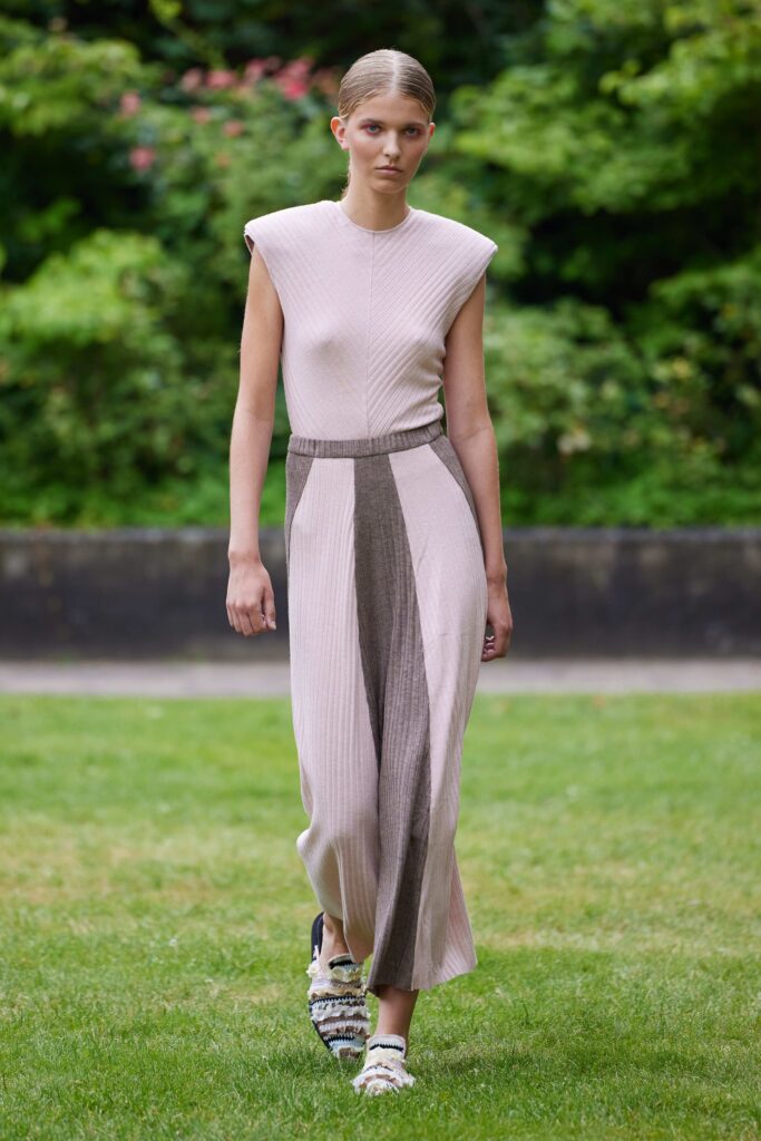 A fitted beige and brown sleeveless dress with an asymmetric design and knee-length hem.