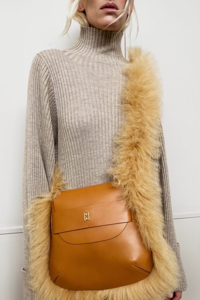 A relaxed beige wool sweater with long sleeves, a turtleneck, and fringed detailing.