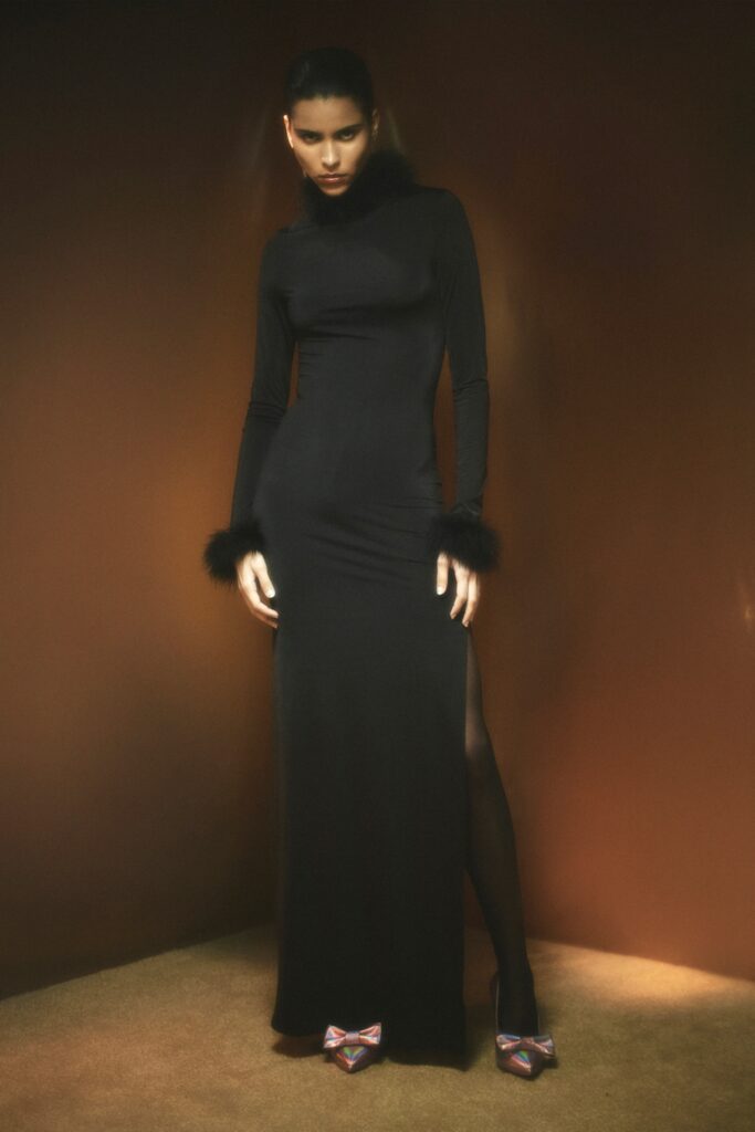 A fitted black silk gown with long sleeves, a high neckline, and a side slit.