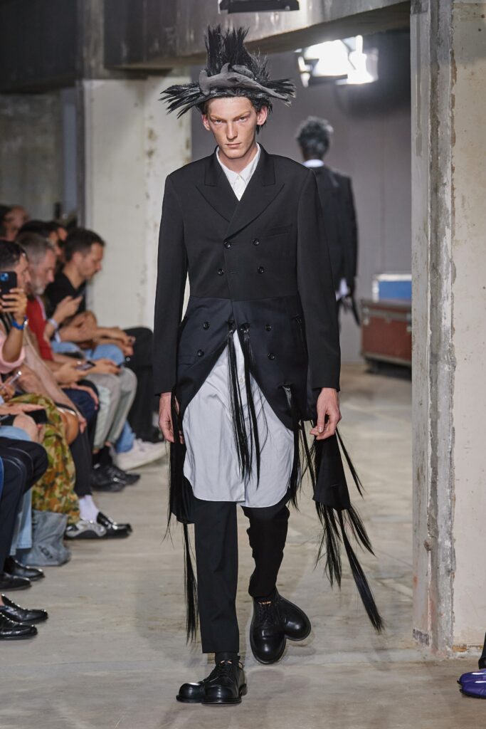 A structured black suit with long sleeves, a collared neckline, and an asymmetric layered design.