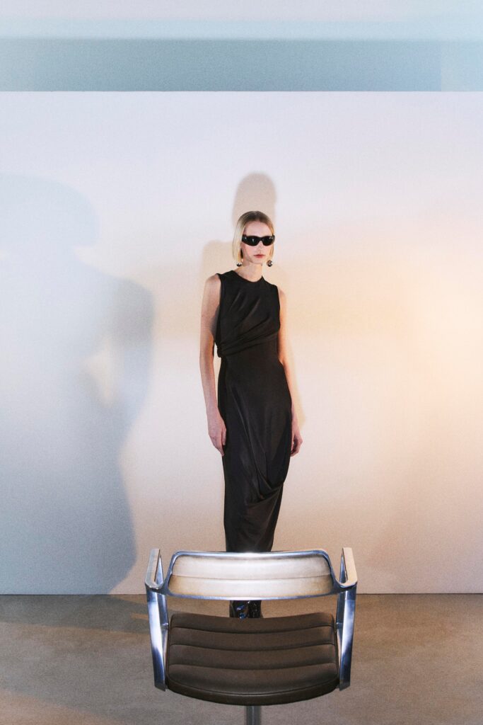 A fitted black silk sleeveless dress with a high neckline and draped design.