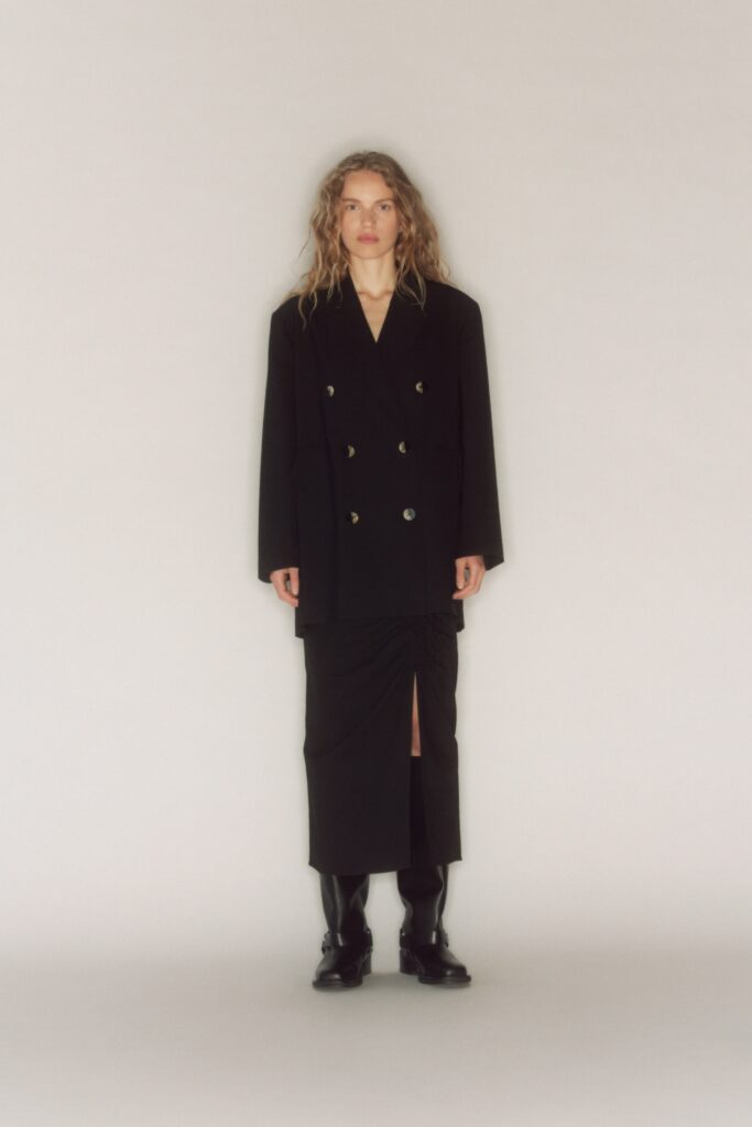 A fitted black blazer with a long sleeve and a black skirt featuring an asymmetric slit.