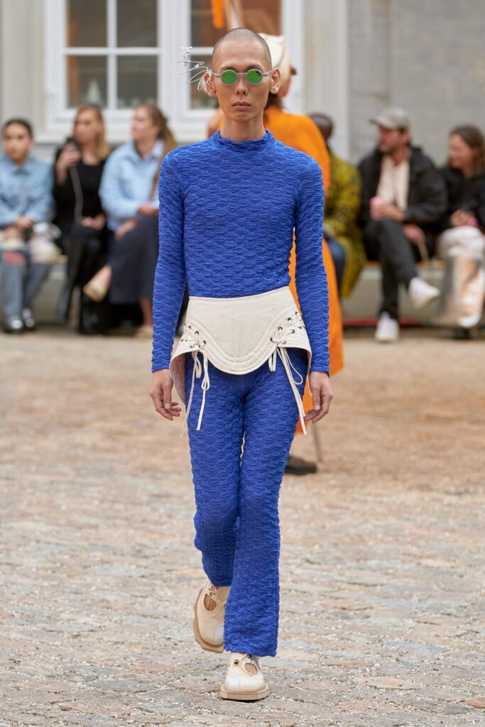 A fitted blue long-sleeve top paired with high-waisted white pants featuring a textured design.
