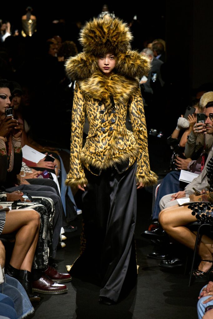 A fitted brown fur coat with a high-neck and long sleeves, paired with a flared black skirt.