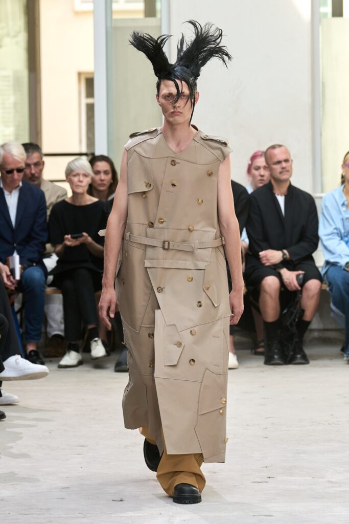 A relaxed beige sleeveless jacket dress with an asymmetric design and button details.