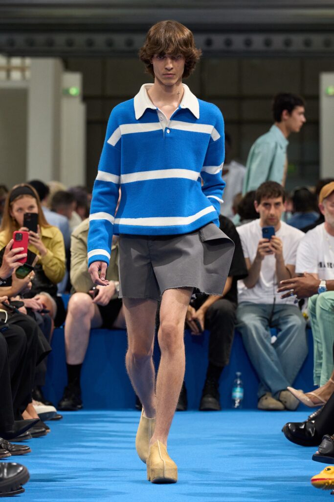 A relaxed blue striped long-sleeve shirt with a collared neckline paired with pleated gray shorts.
