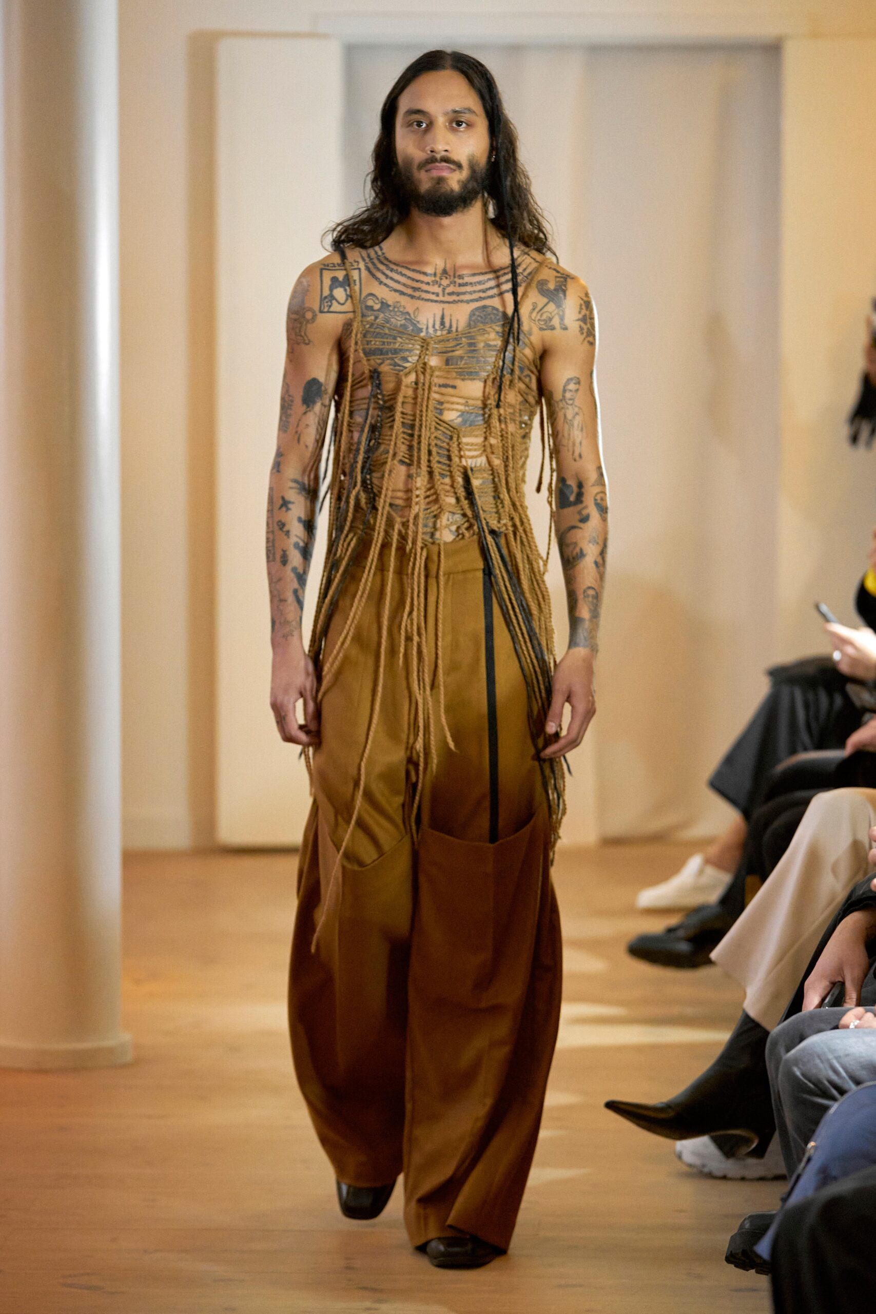 A relaxed brown and beige sleeveless top with asymmetric details paired with layered pants.