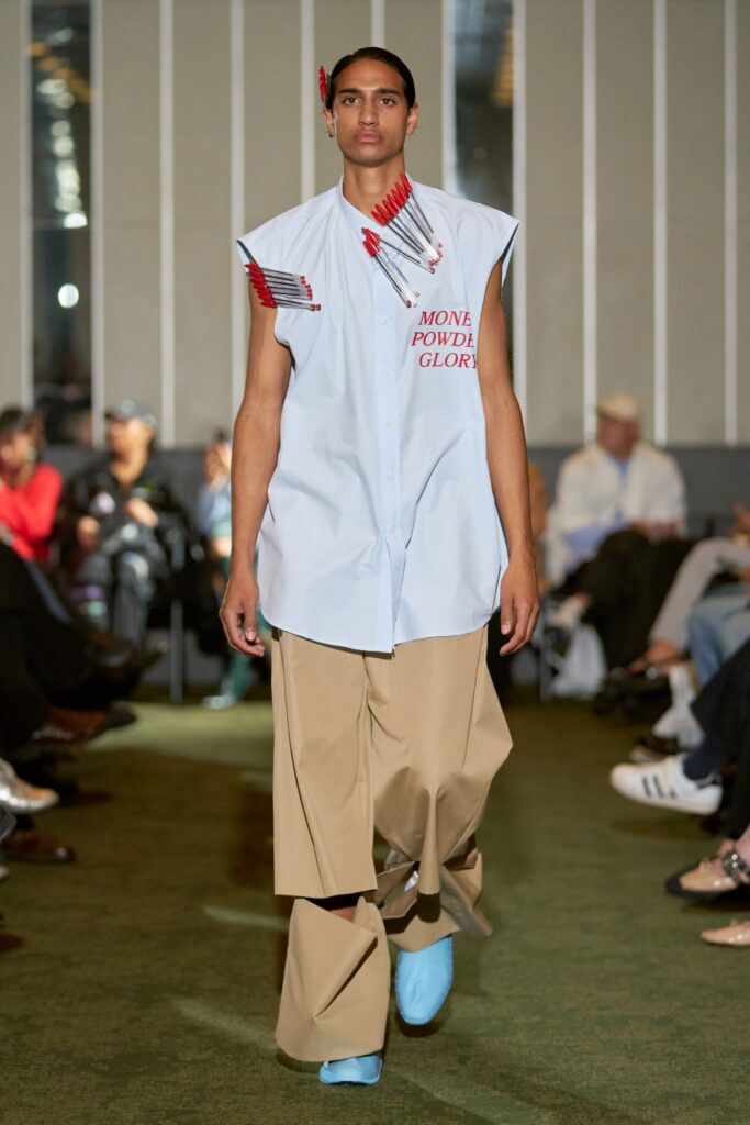An oversized blue collared shirt with printed details paired with wide-leg beige pants.