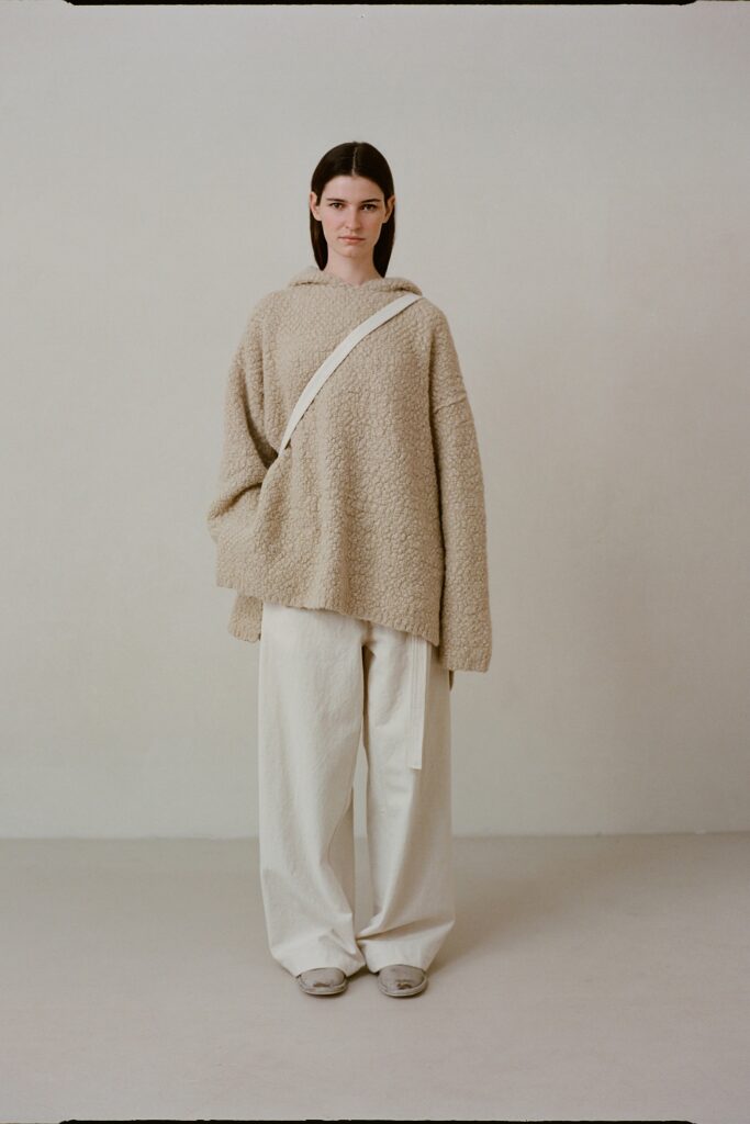 An oversized beige sweater with long sleeves paired with white pants, featuring a textured design.