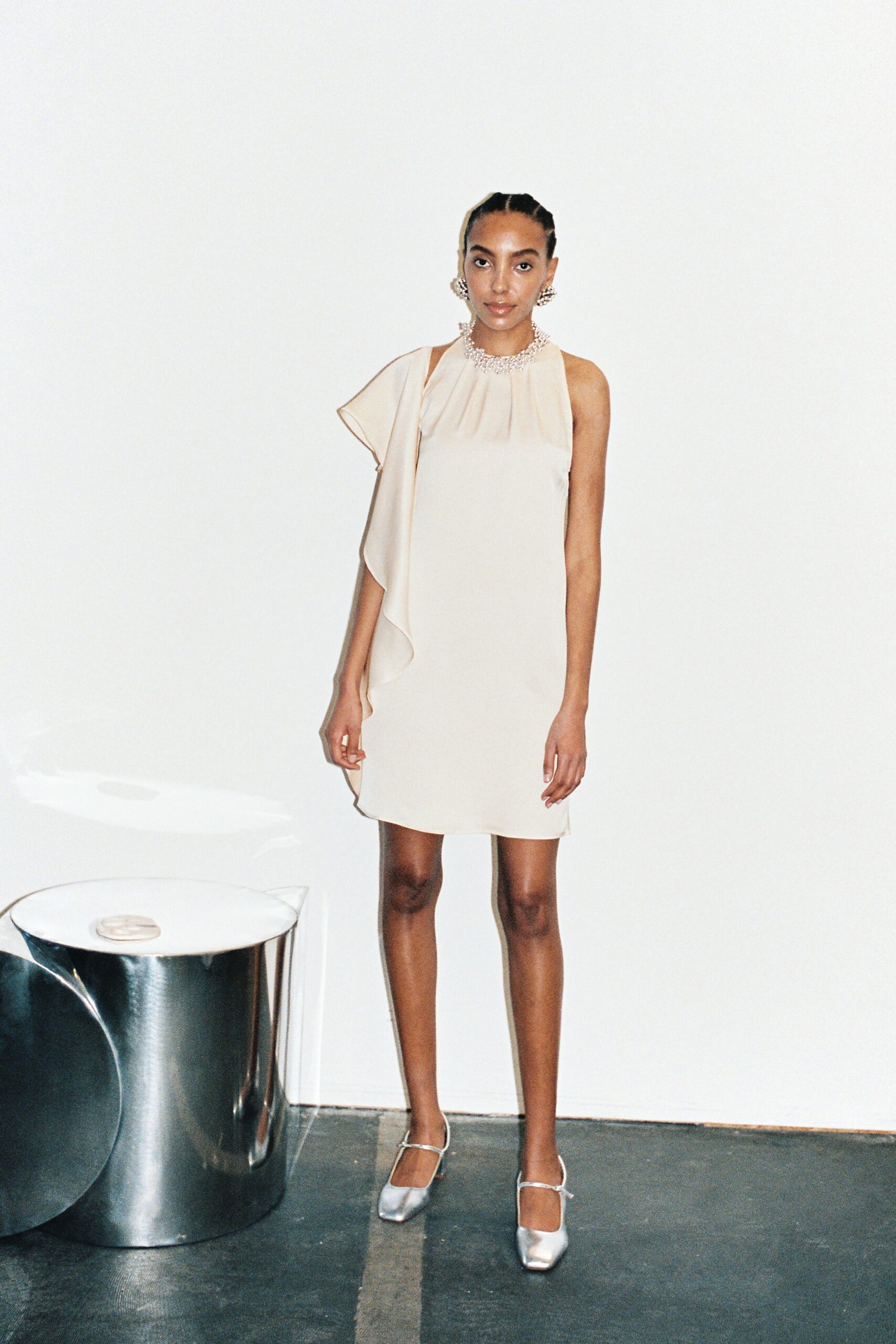 A fitted beige silk dress with a sleeveless design and asymmetric detail.