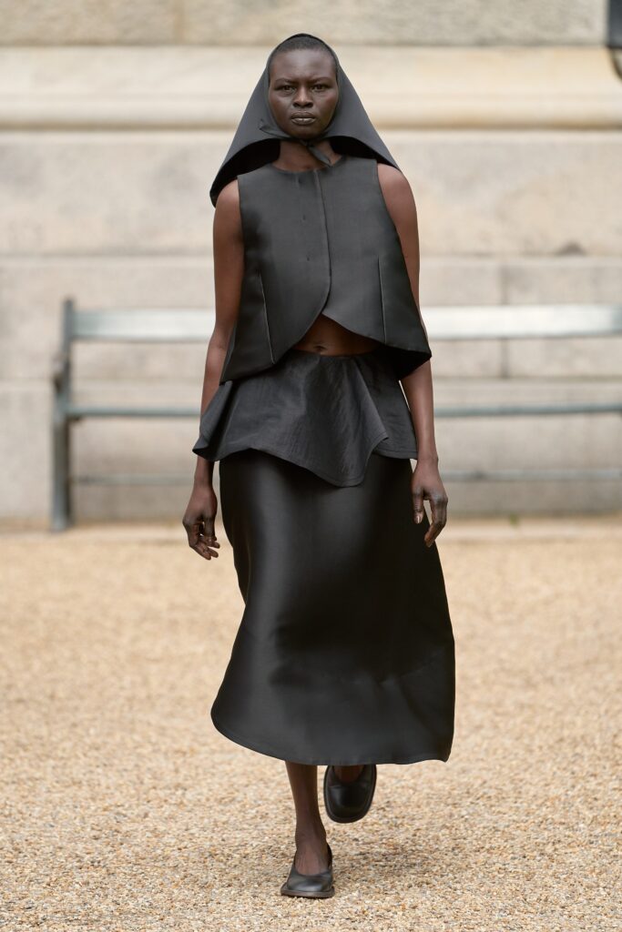 A fitted black dress with an asymmetric design and high-neck construction, showcasing modern elegance.