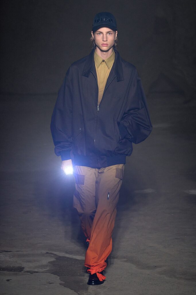 An oversized black jacket paired with straight-leg orange pants featuring a zippered detail.