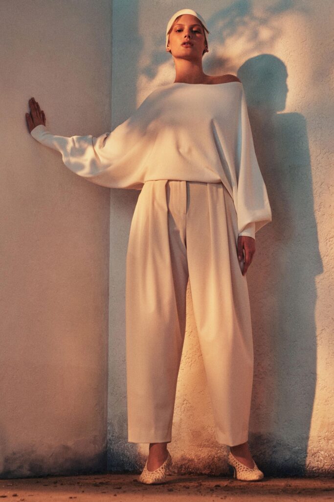A relaxed white off-shoulder top paired with pleated pants for a stylish look.