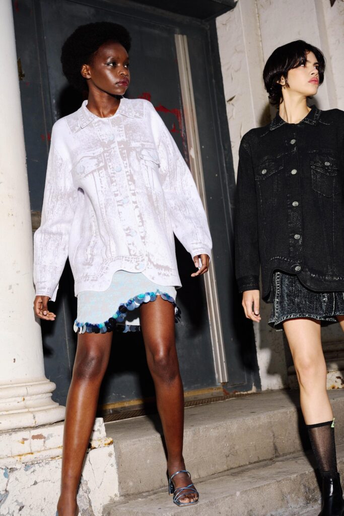 A relaxed black denim jacket paired with a white dress featuring layered and fringed details.