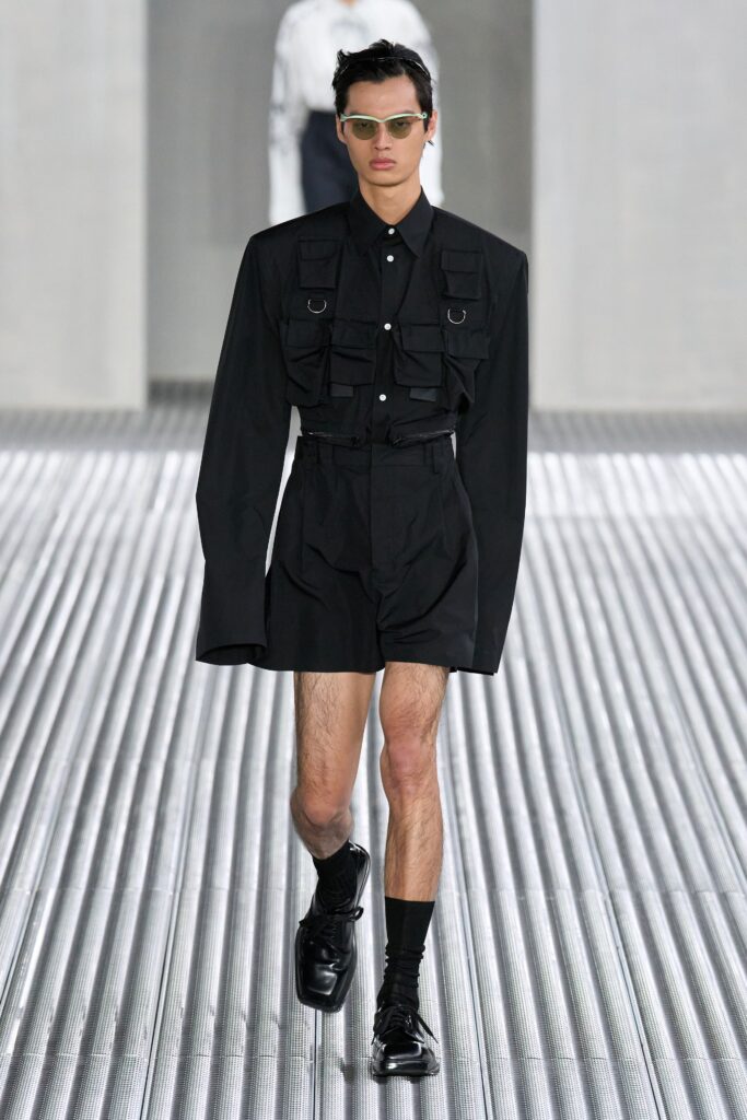 A fitted black cotton shirt with long sleeves and pleated shorts, featuring a collared design.