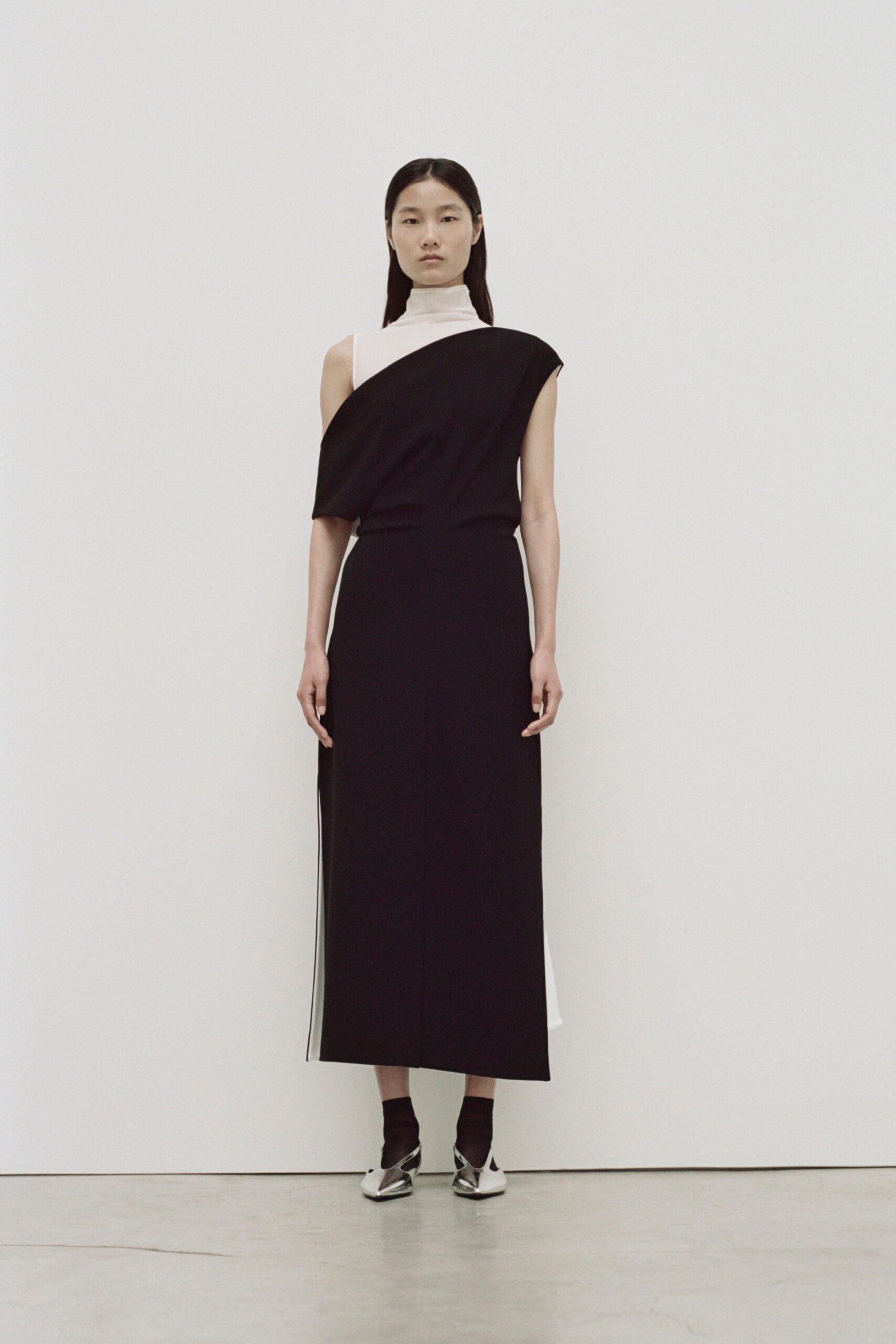A fitted black and white sleeveless dress with a high neckline and asymmetric design.