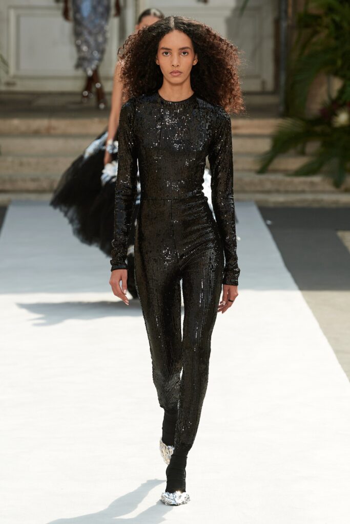 A fitted black sequin catsuit with long sleeves and a high neckline, featuring a straight-leg design.